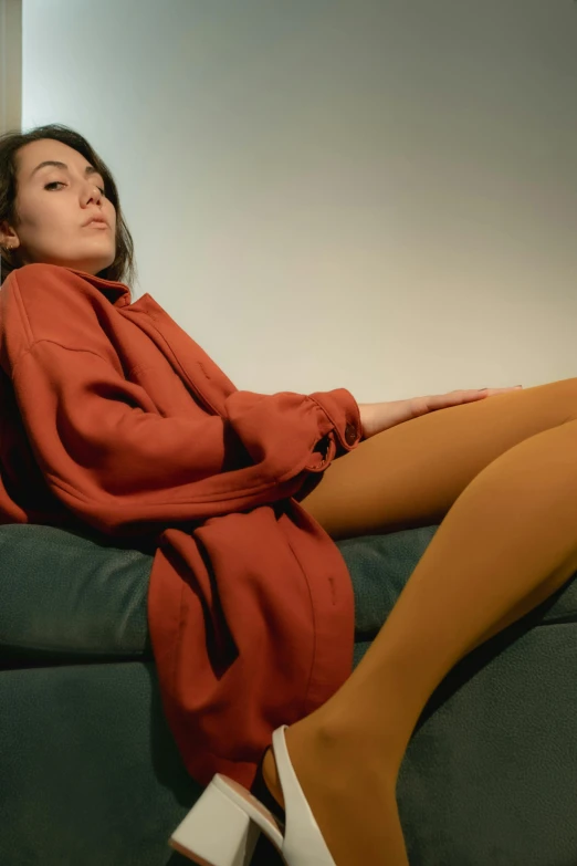 a woman sitting on top of a green couch, inspired by Elsa Bleda, trending on pexels, hyperrealism, long orange sweatshirt, pantyhose tights, wearing red and yellow clothes, caramel. rugged