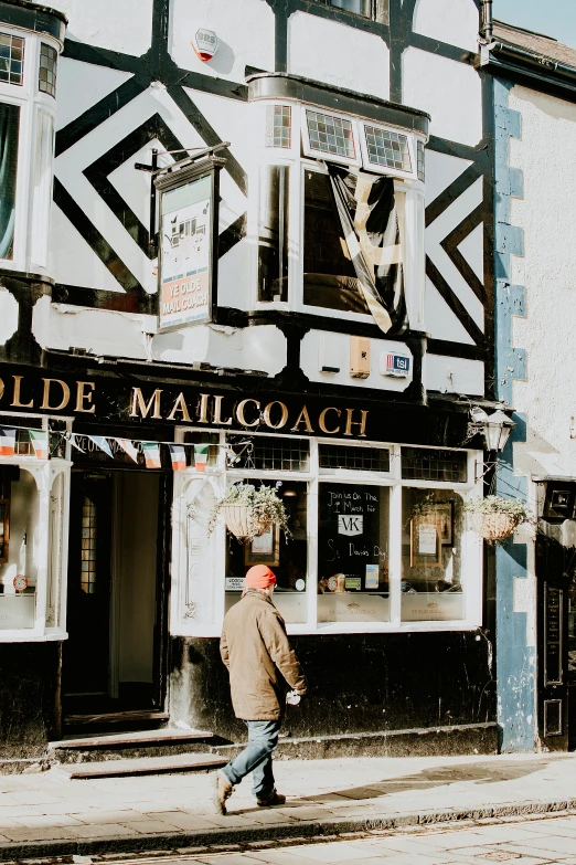 a man walking down a street past a building, in the pub, delivering mail, goldilocks, old town