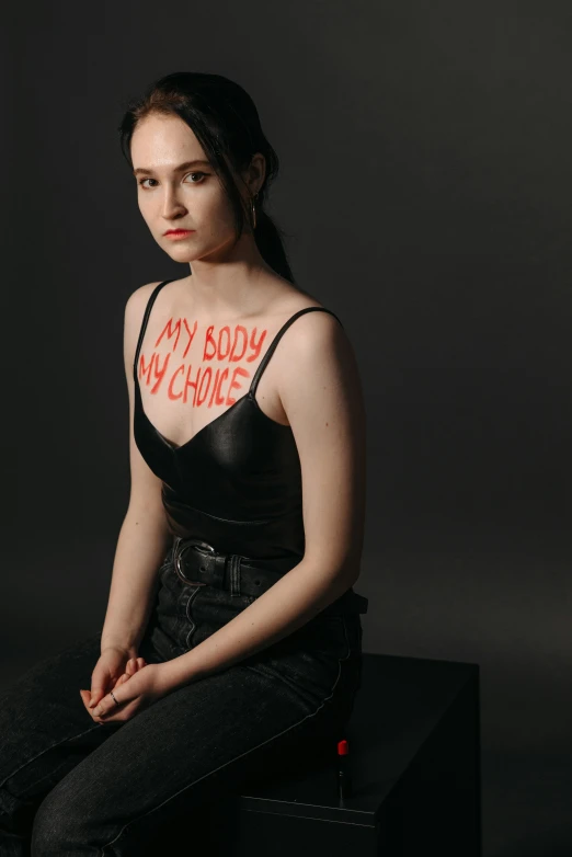 a woman sitting on top of a black box, an album cover, by Winona Nelson, featured on reddit, red leather corset, with pale skin, woman holding sign, crop top