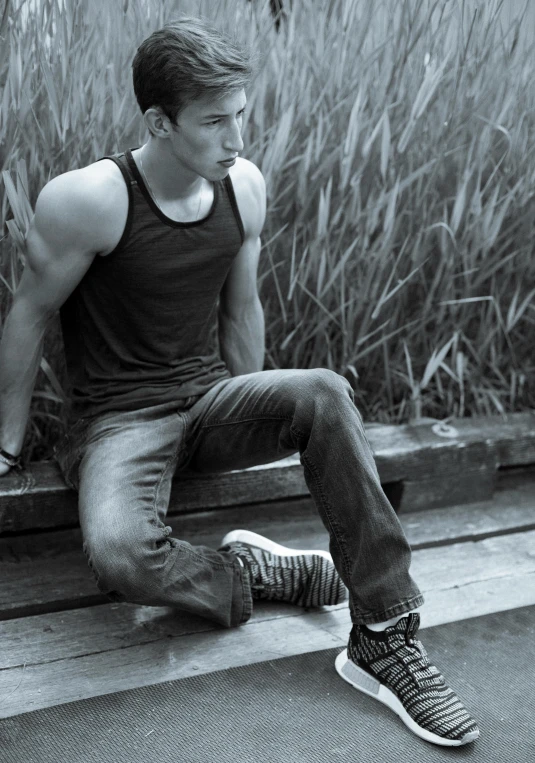 a black and white photo of a man sitting on a bench, wearing tank top, cute young man, ayne haag, jeans and t shirt