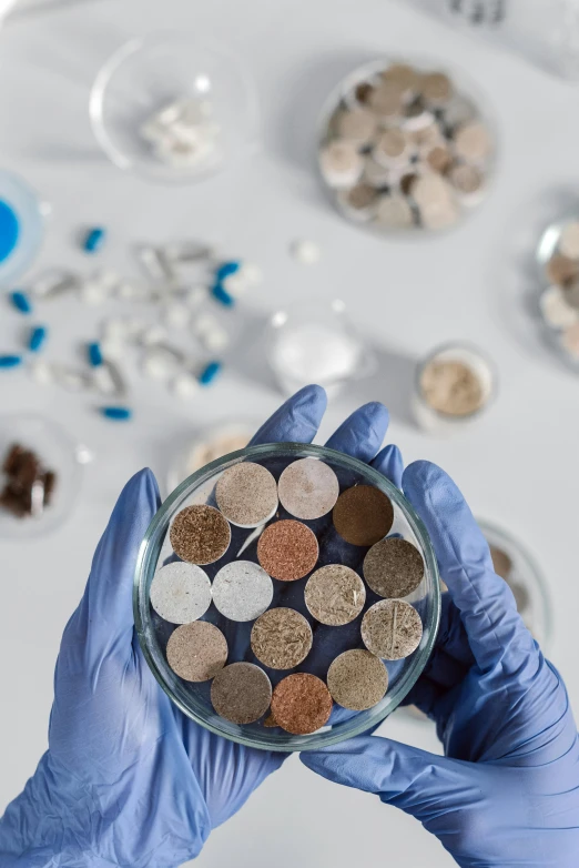 a person in blue gloves holding a bowl of coins, a microscopic photo, plasticien, metal rust and plaster materials, high samples, ai biodiversity, brown