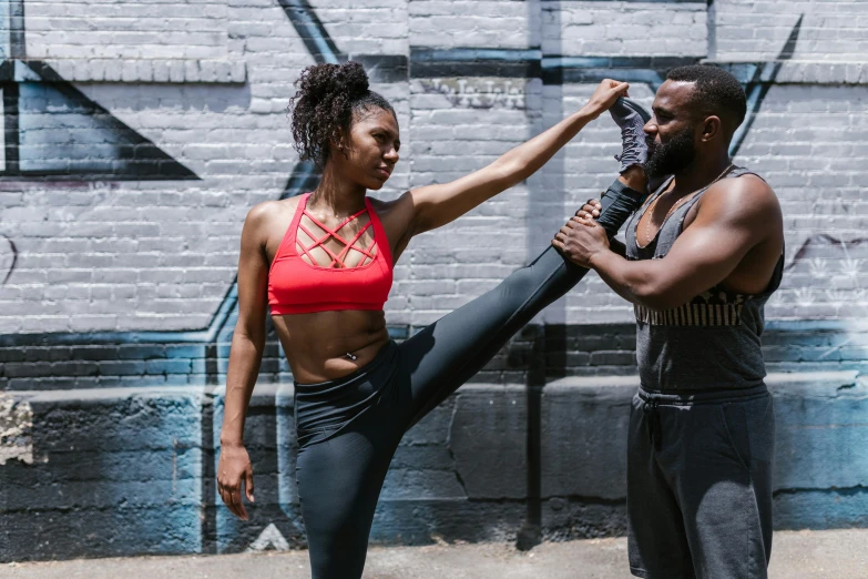 a man and a woman standing in front of a graffiti wall, by Nina Hamnett, pexels contest winner, black arts movement, doing splits and stretching, cropped red yoga short, athletic crossfit build, cast