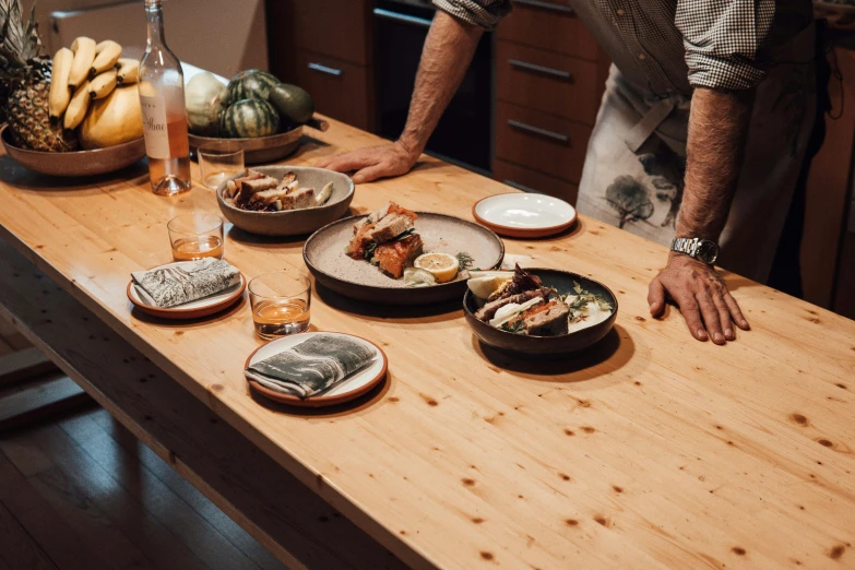 a man standing in front of a table filled with plates of food, a still life, unsplash, private press, raku, on wooden table, dwell, close up details