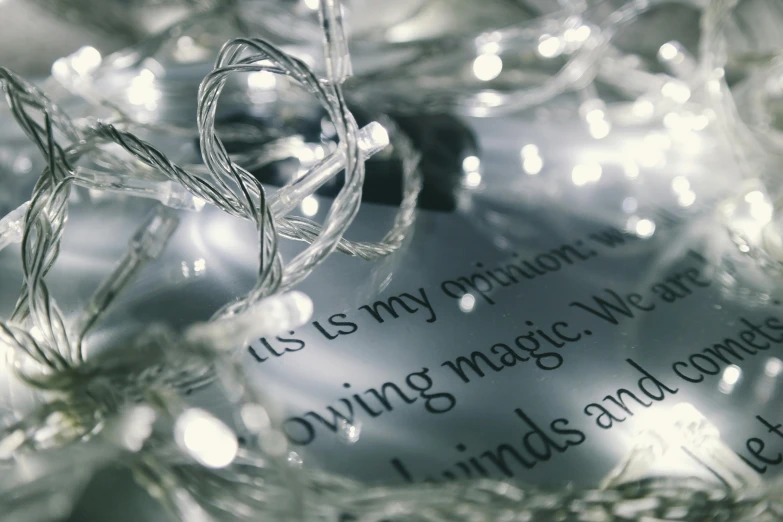 a close up of a christmas ornament on a table, inspired by Cerith Wyn Evans, unsplash, magical realism, detailed string text, open magic book glowing, grey and silver, made of glass