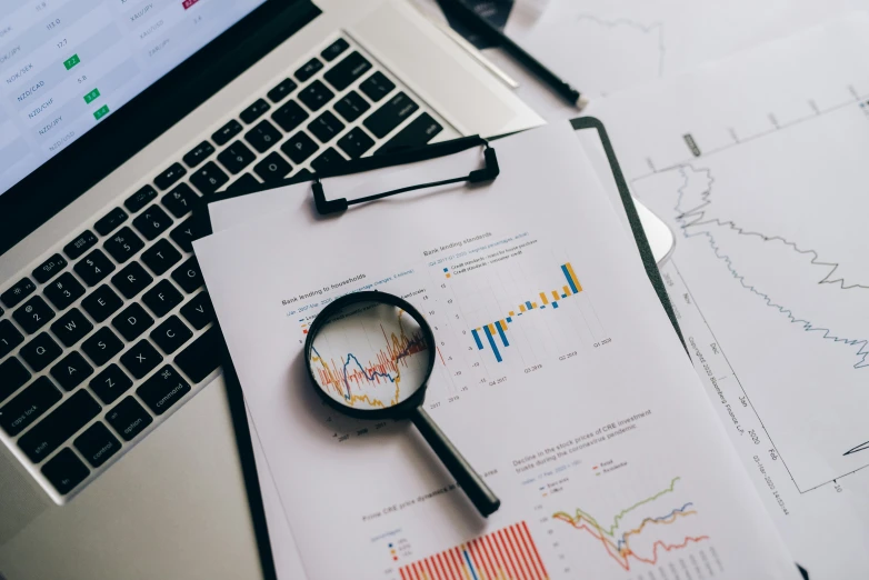 a laptop computer sitting on top of a desk next to a magnifying glass, a screenshot, trending on unsplash, analytical art, graphs, papers on table, 🦩🪐🐞👩🏻🦳, uncropped