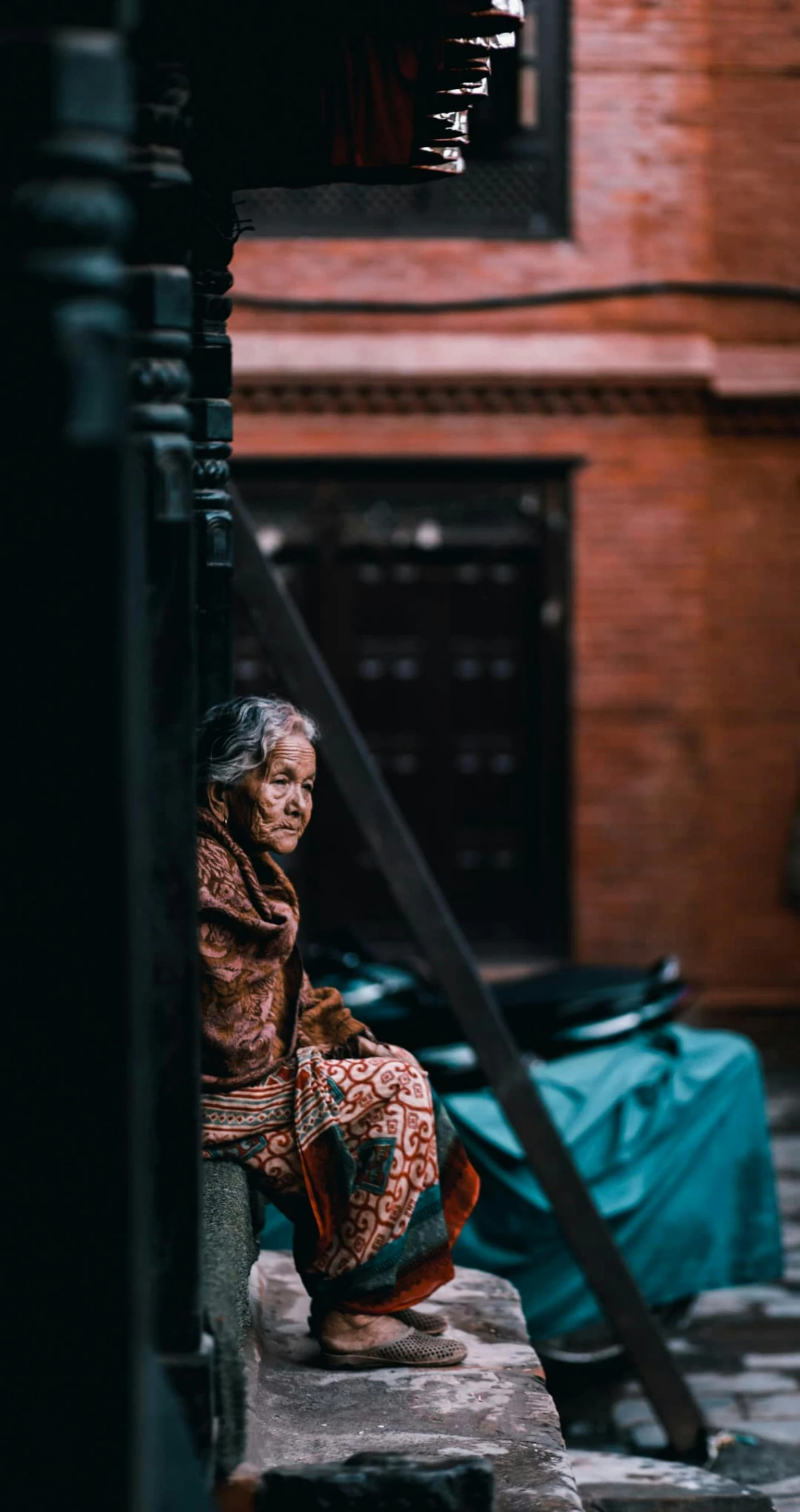 a woman sitting on the steps of a building, pexels contest winner, hurufiyya, an old lady with red skin, people waiting in bus stop, nepali architecture buildings, unsplash 4k