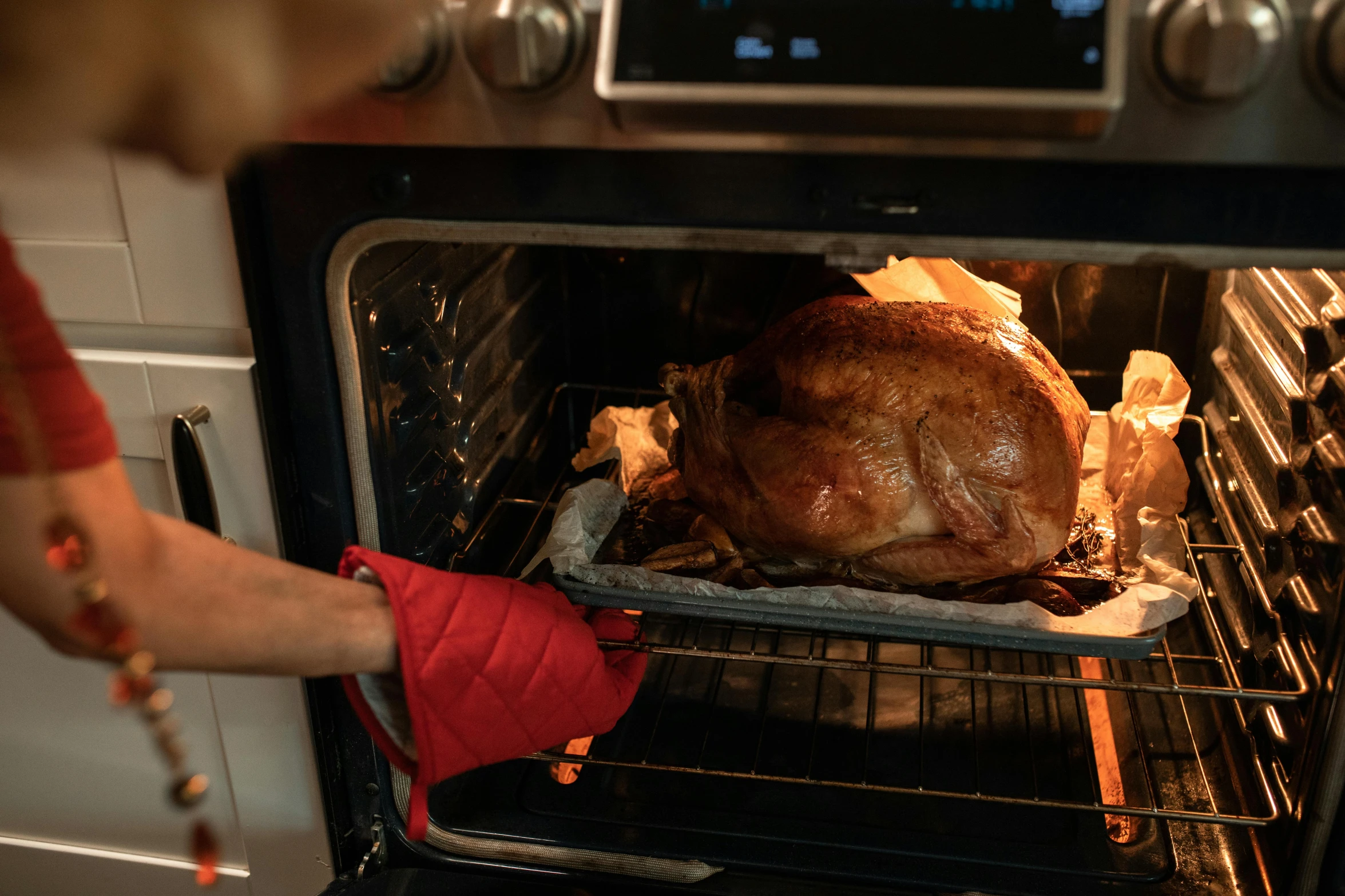 a woman taking a turkey out of the oven, red gloves, connectivity, press shot, angled shot