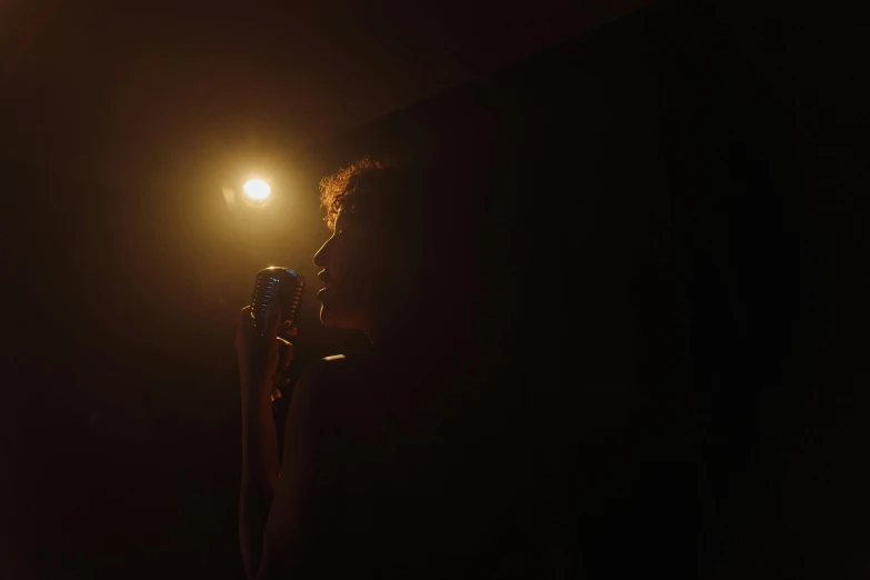 a woman singing into a microphone in the dark, inspired by Nan Goldin, minimalist cinematic lighting, medium-shot, clemens ascher, taken with sony alpha 9