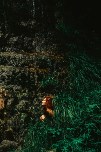 a woman standing in front of a waterfall, inspired by Elsa Bleda, hiding in grass, ( redhead, cave wall, a high angle shot