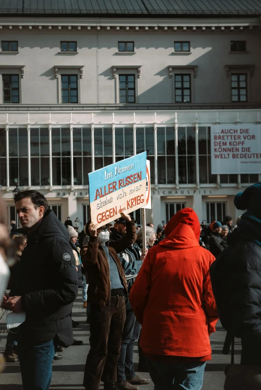 a crowd of people standing in front of a building, subject action: holding sign, berlin fashion, thumbnail, winter