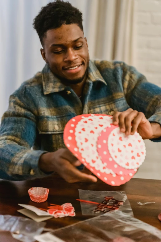 a man sitting at a table holding a heart shaped box, pexels contest winner, plasticien, african canadian, polka dot tables, instruction, over a dish and over a table