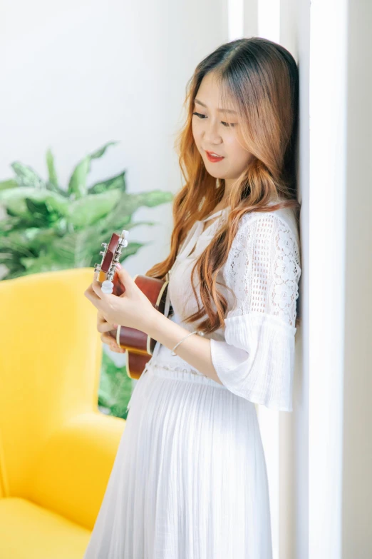 a woman standing next to a yellow couch holding a guitar, inspired by Huang Ji, pexels contest winner, wearing white dress, ulzzang, profile pic, on white