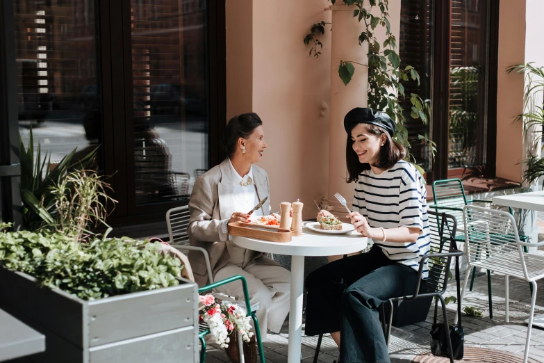 a man and a woman sitting at a table, by Emma Andijewska, pexels contest winner, eating outside, two women, wearing a french beret, full body image