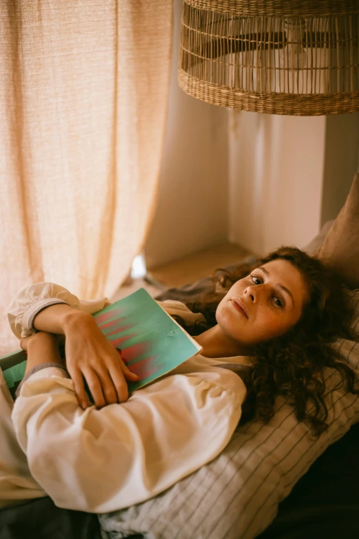 a woman laying on a bed reading a book, an album cover, inspired by Elsa Bleda, pexels contest winner, happening, young middle eastern woman, holding notebook, soft sunbeam, wavy hair spread out