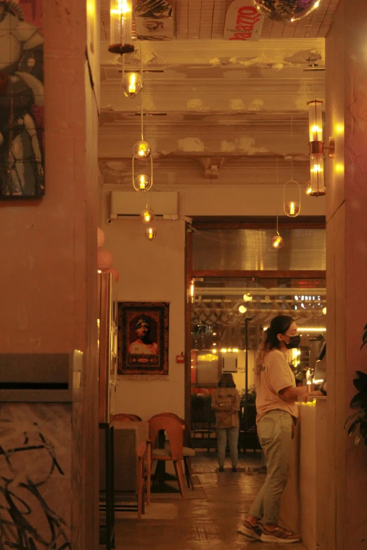 a woman standing at a counter in a restaurant, a picture, unsplash, art nouveau, warm street lights store front, orthodox, cuban setting, yellow lighting from right