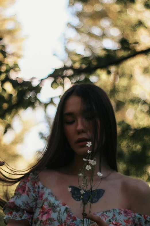 a woman in a floral dress holding a flower, inspired by Elsa Bleda, pexels contest winner, aestheticism, young woman with long dark hair, blurred, next to a tree, portrait sophie mudd