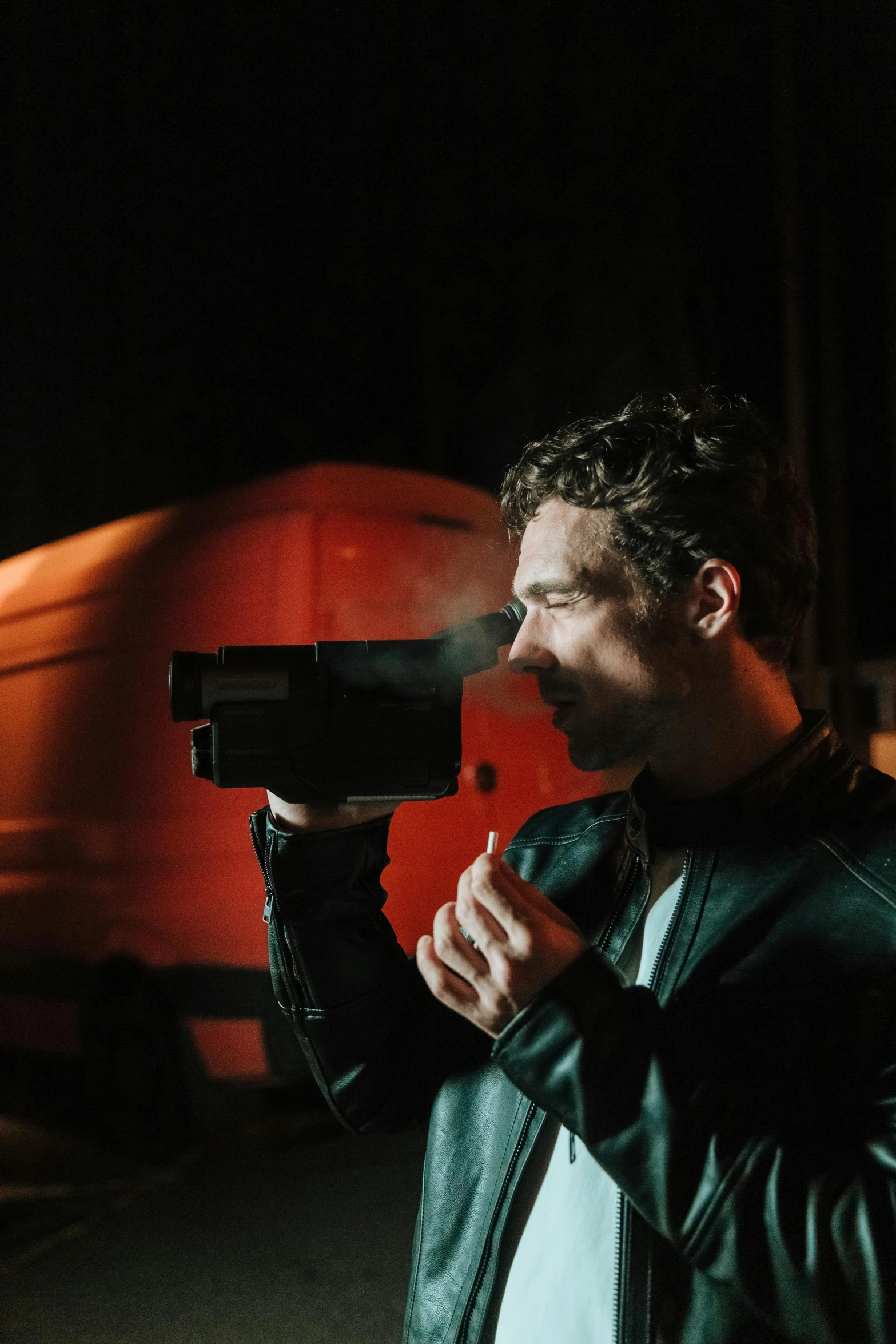 a man in a leather jacket holding a video camera, inspired by roger deakins, robert sheehan, taking a smoke break, at nighttime, vhs recording