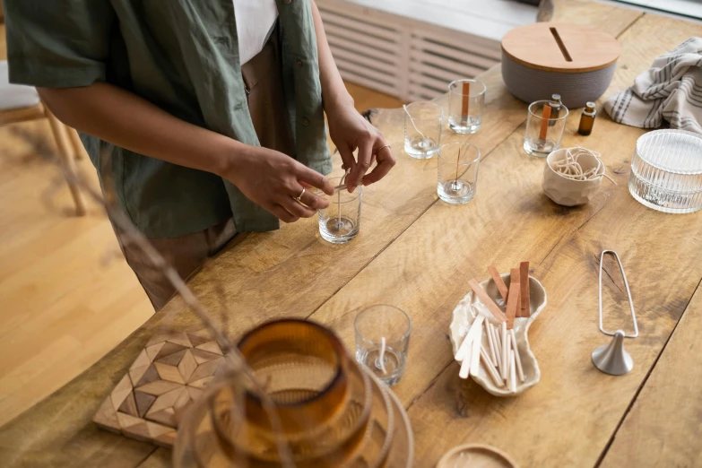 a woman preparing food on a wooden table, a still life, trending on pexels, process art, glass vials, wood cups, brown, drinking