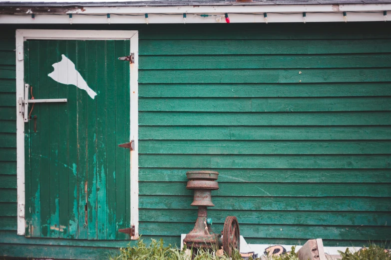 a green building with a green door and a fire hydrant, an album cover, unsplash, weathered artifacts, cottage, shed, anthony mcbain