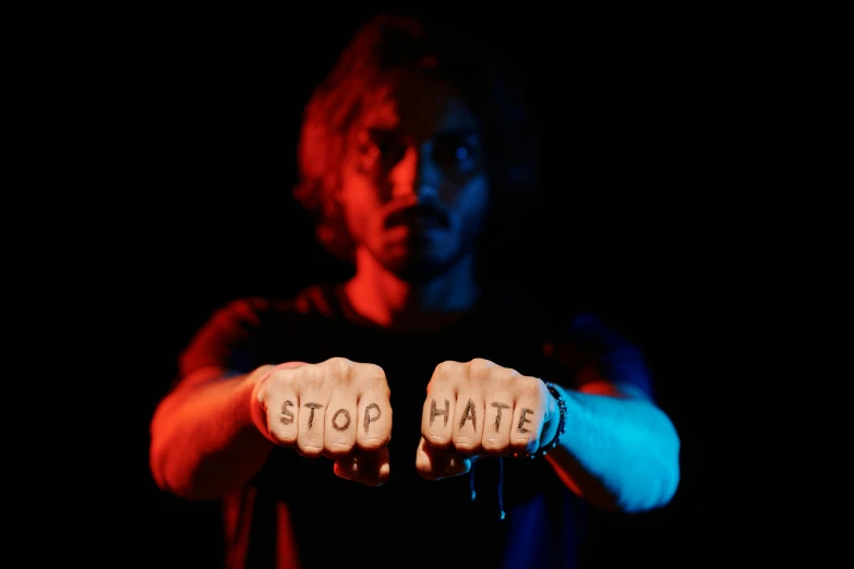 a man with the word stop hate written on his hands, an album cover, pexels, sots art, phosphorescent, joe keery, college, chromatic