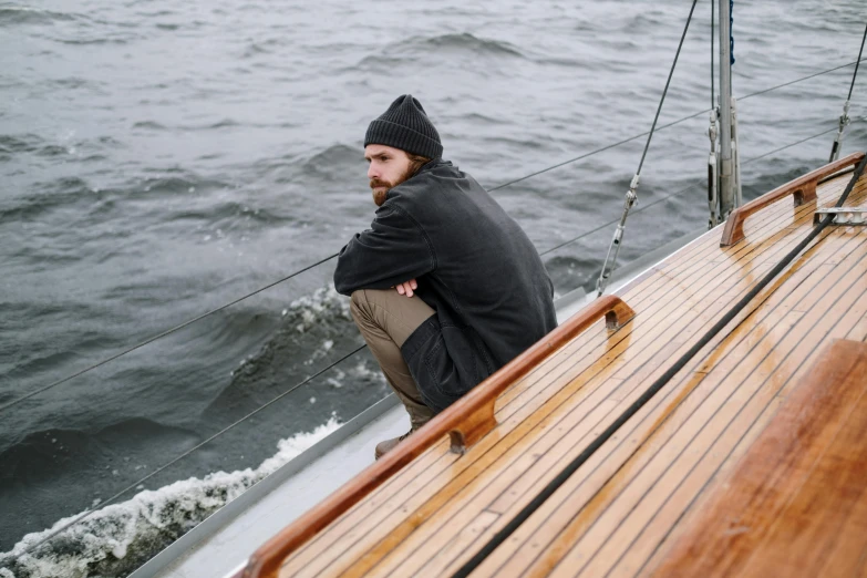 a man is sitting on the deck of a boat, a portrait, by Caspar Wolf, pexels contest winner, purism, wearing a grey hooded sweatshirt, disappointed, 1 2 9 7, sailboat