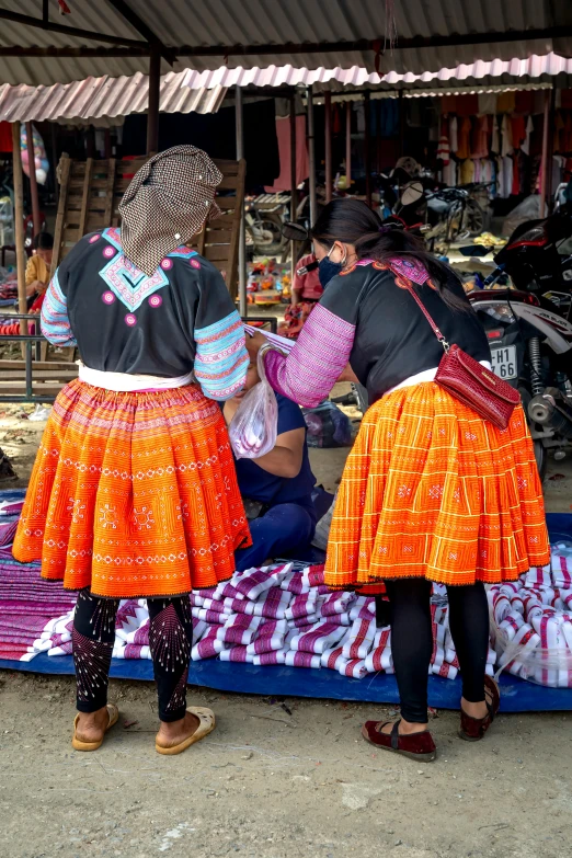 a couple of women standing next to each other, tribal clothing, market setting, in style of lam manh, facing away