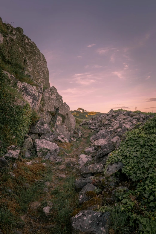 a group of rocks sitting on top of a lush green hillside, an album cover, by Filip Hodas, unsplash, explorers of the ruins at dusk, cornwall, narrow footpath, panoramic