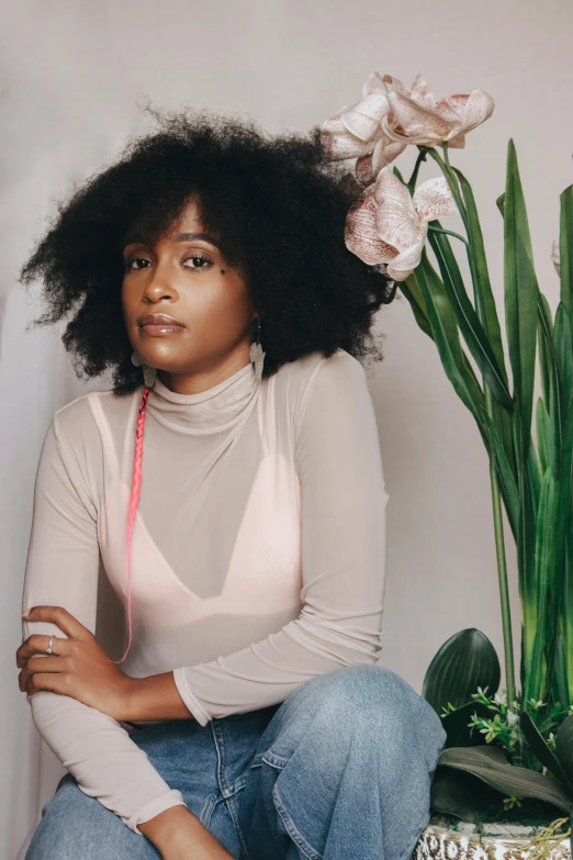 a woman sitting next to a potted plant, an album cover, by Lily Delissa Joseph, natural hair, wearing a turtleneck and jacket, portrait soft light, flowers