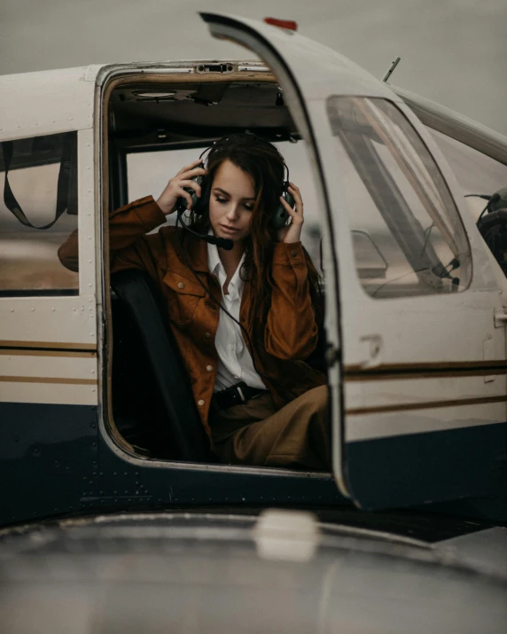 a woman sitting in the cockpit of a small airplane, by Christen Dalsgaard, trending on unsplash, giant headphones rocking out, an aviator jacket and jorts, helicopters, leaving a room