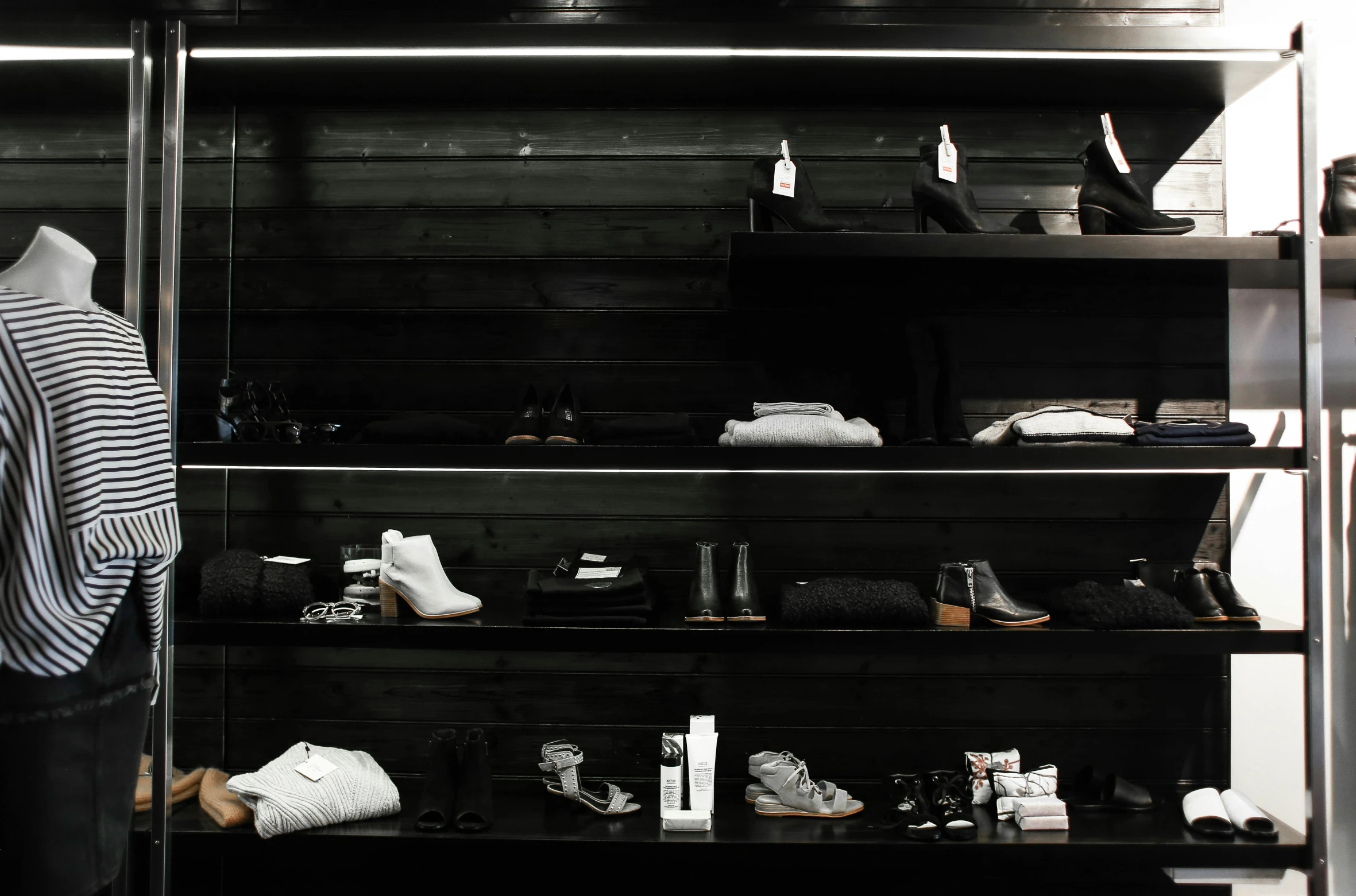 a person standing in front of a rack of shoes, a black and white photo, unsplash, minimalism, skincare, dark garments, sitting on a store shelf, white clothing