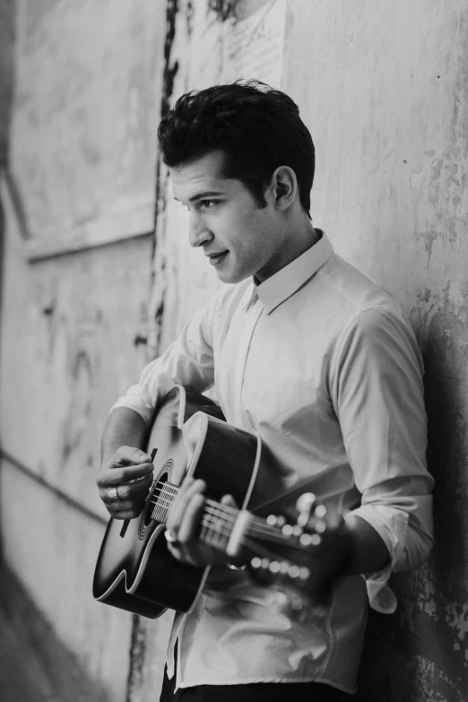 a man with a guitar leaning against a wall, by Alejandro Obregón, he is about 2 0 years old, singing for you, dany devito, sayem reza