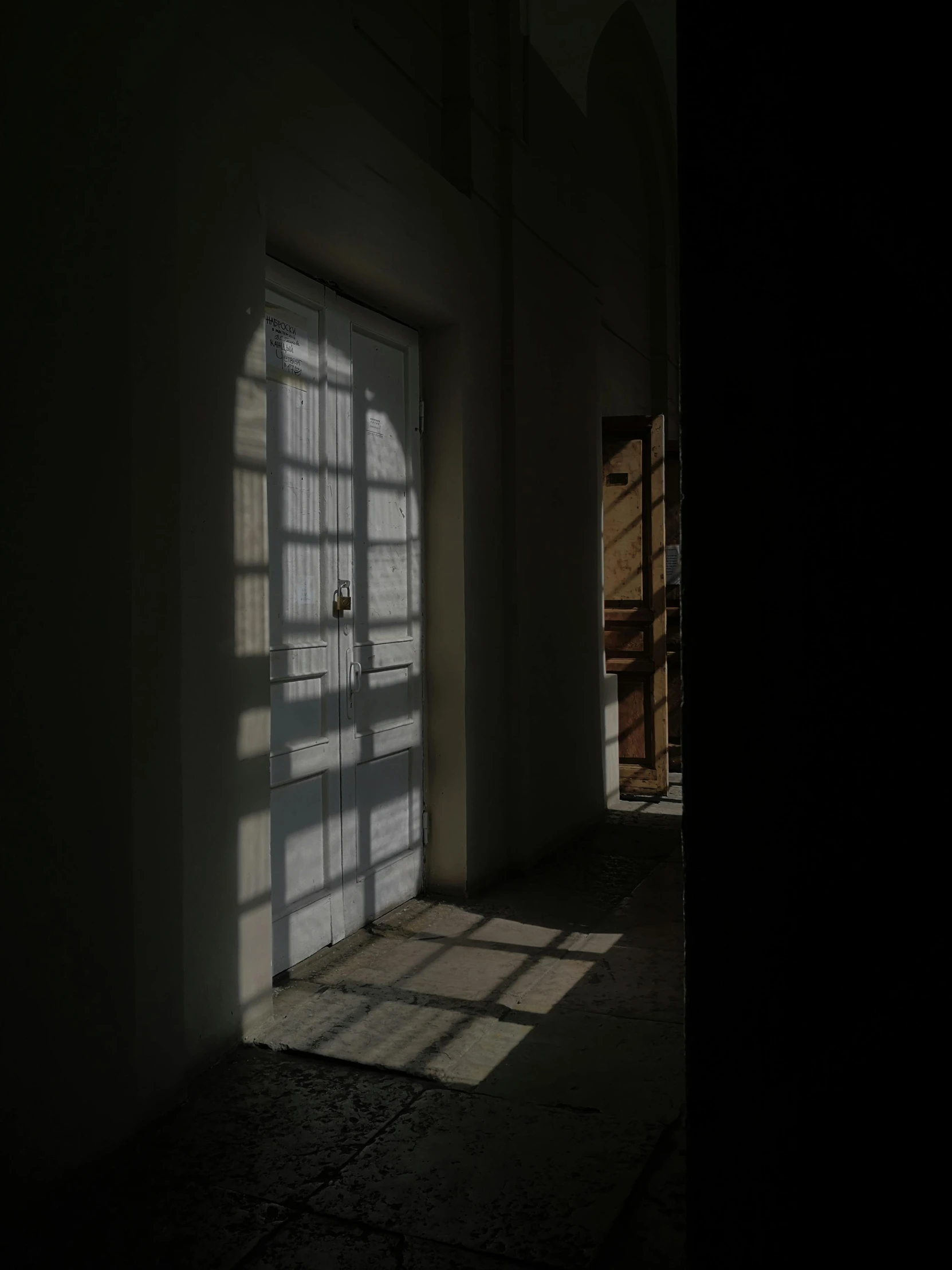 the sun shines through a window in a dark room, inspired by Pieter de Hooch, light and space, taken on iphone 14 pro, old jeddah city alley, door, inside white room