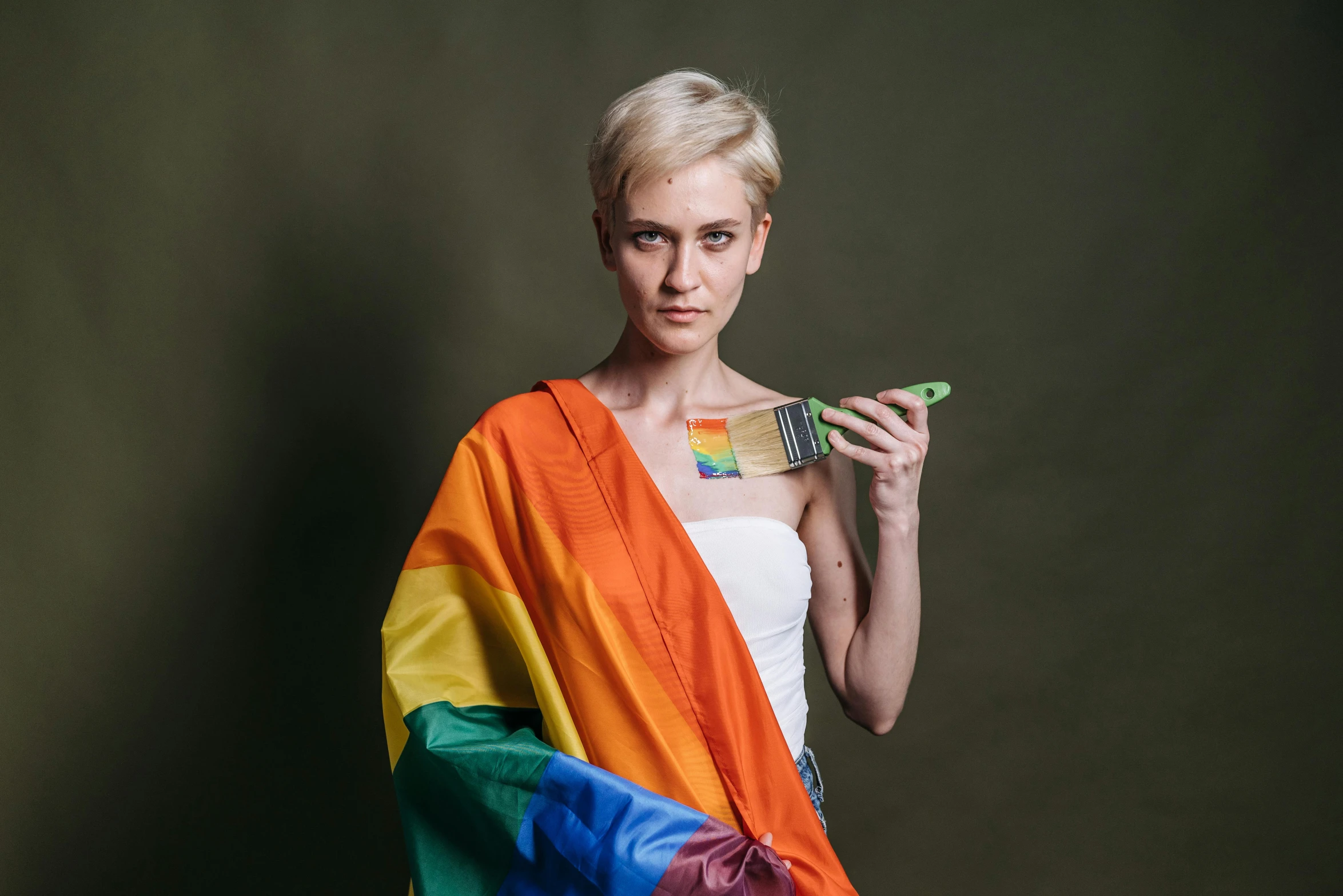 a woman in a white dress holding a rainbow flag, inspired by Anna Füssli, holding a paintbrush in his hand, non binary model, blonde woman, owen gent