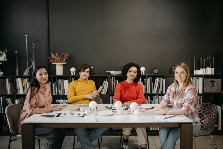 three women sitting at a table in front of a bookshelf, a portrait, pexels contest winner, academic art, clay animation, white wall coloured workshop, group sit at table, avatar image