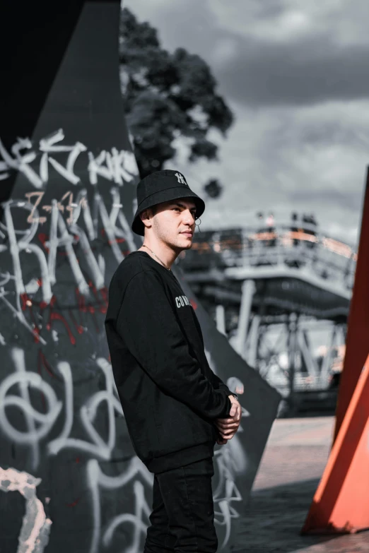 a man standing in front of a graffiti covered wall, black beanie, vitaly bugarov, discord profile picture, low quality photo