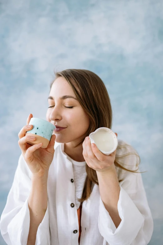 a woman sitting at a table drinking out of a cup, trending on pexels, white and pale blue, smelling good, high quality product image”, studio photo