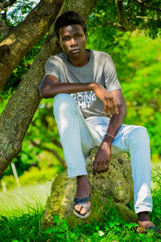 a man sitting on top of a rock under a tree, a picture, by Camille-Pierre Pambu Bodo, happening, headshot profile picture, adut akech, college, lush green