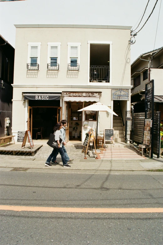 a couple of people walking down a street, shin hanga, small hipster coffee shop, white building, in 2 0 0 2, a quaint