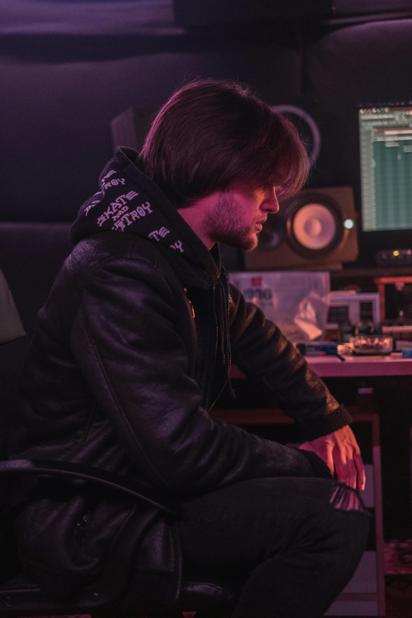 a man sitting at a desk in front of a computer, an album cover, by Jacob Toorenvliet, trending on pexels, in a black hoodie, studio lights, sitting at a control center, wearing jacket