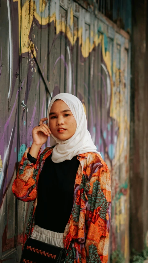 a woman standing in front of a graffiti covered wall, inspired by Bernardino Mei, pexels contest winner, white hijab, in front of an orange background, 15081959 21121991 01012000 4k, batik