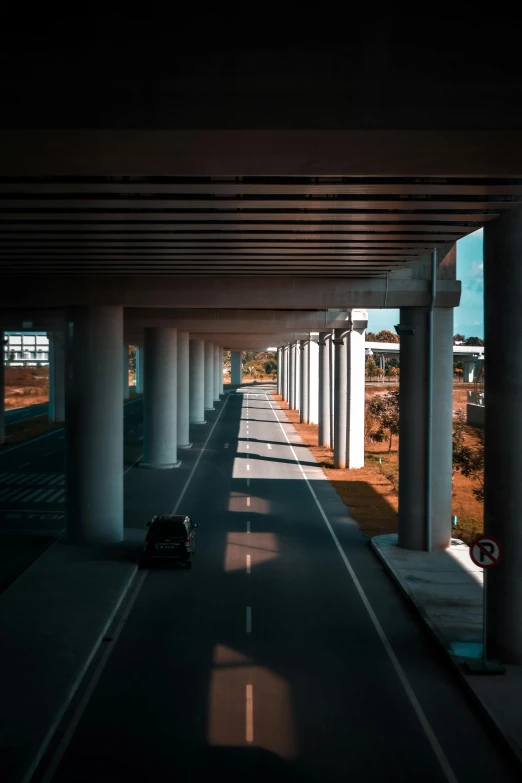 a car driving down a highway under a bridge, by Jacob Toorenvliet, unsplash contest winner, conceptual art, tall columns, walking through a suburb, shadows, cars parked underneath