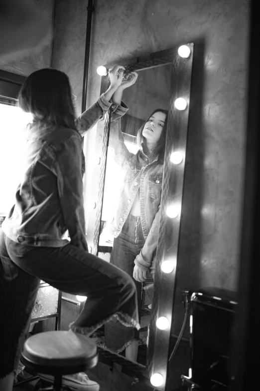 a woman sitting on a stool in front of a mirror, a black and white photo, by Dave Melvin, iggy pop, exiting from a wardrobe, cowgirl, flashing lights