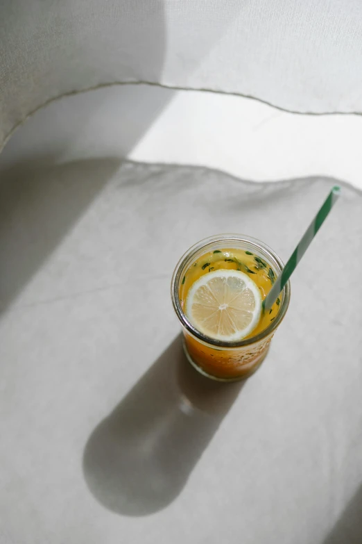 a glass of orange juice sitting on top of a table, by Matthias Stom, trending on unsplash, green tea, sun puddle, with a straw, grey orange