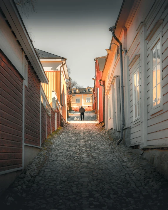 a person walking down a cobblestone street, by Jesper Knudsen, pexels contest winner, swedish houses, glowy light, swedish countryside, colonial era street