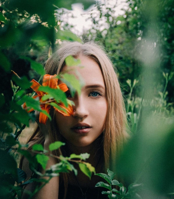 a woman holding a flower in front of her face, inspired by Elsa Bleda, unsplash, blond hair green eyes, in jungle, 5 0 0 px models, teen girl