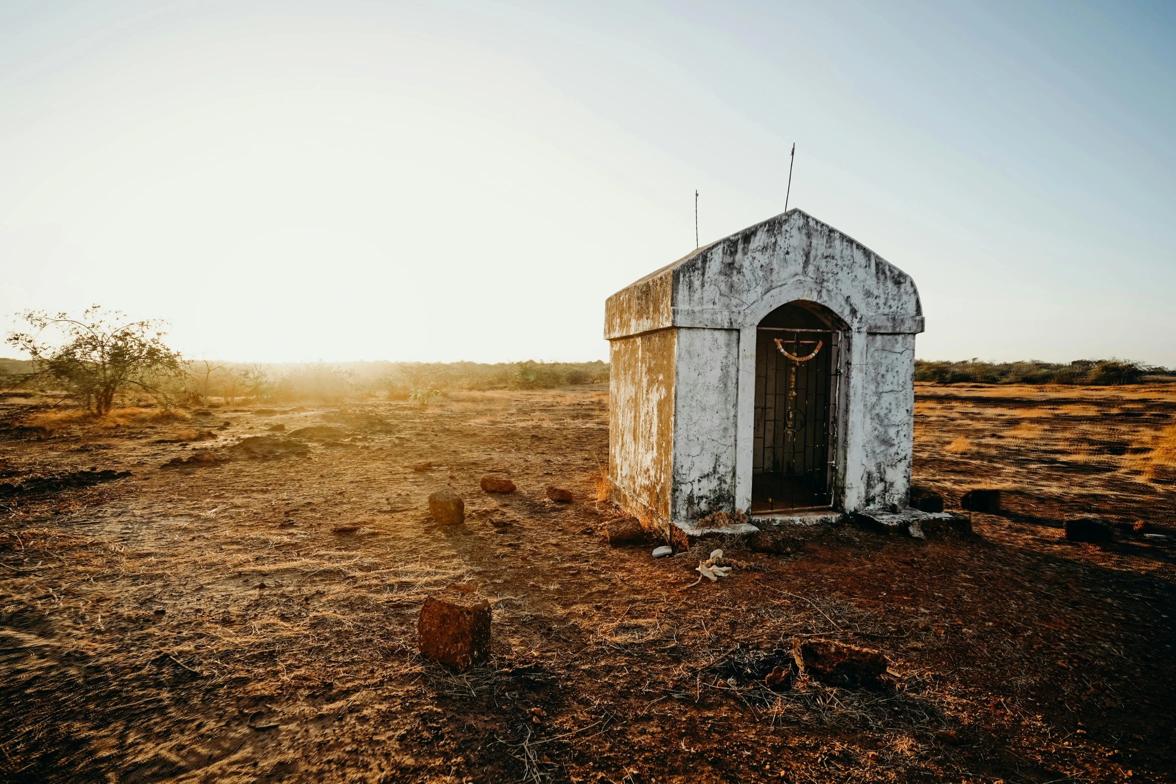 a small white building sitting in the middle of a field, unsplash contest winner, in an ancient altar, in the australian outback, wooden toilets, golden hour photo