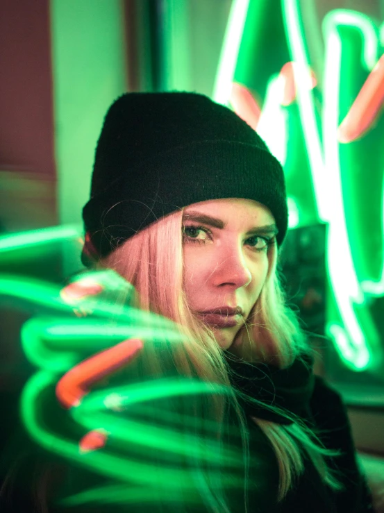 a woman standing in front of a neon sign, a picture, inspired by Elsa Bleda, trending on pexels, synchromism, green hat, blond hair green eyes, glowing lens flare wraith girl, portait photo profile picture