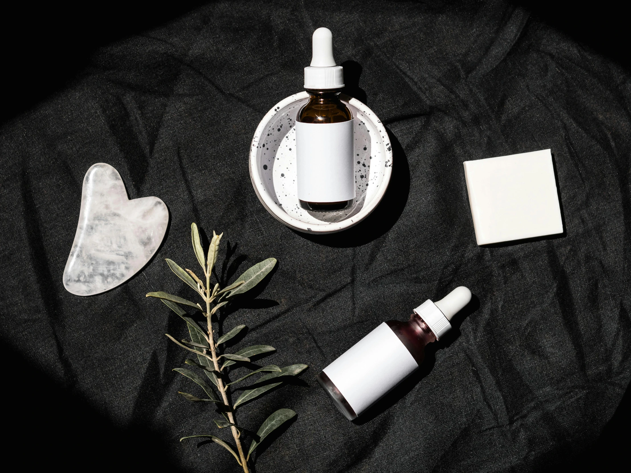 a bottle of liquid sitting on top of a black cloth, by Julia Pishtar, trending on pexels, small vials and pouches on belt, organic ceramic white, eucalyptus, her face is coated in a white