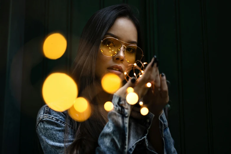 a woman holding a string of lights in front of her face, inspired by Elsa Bleda, pexels contest winner, wearing gold glasses, portrait of vanessa morgan, instagram picture, girl under lantern