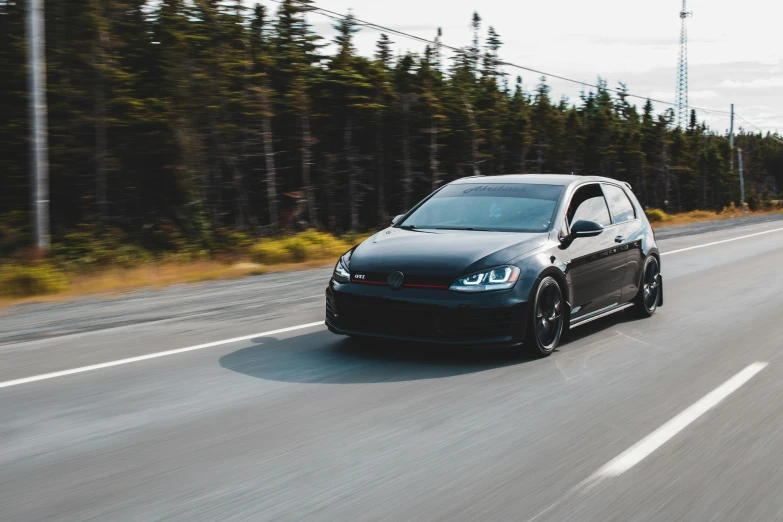 a black car driving down a road next to a forest, racecar, avatar image, vehicles, detailing